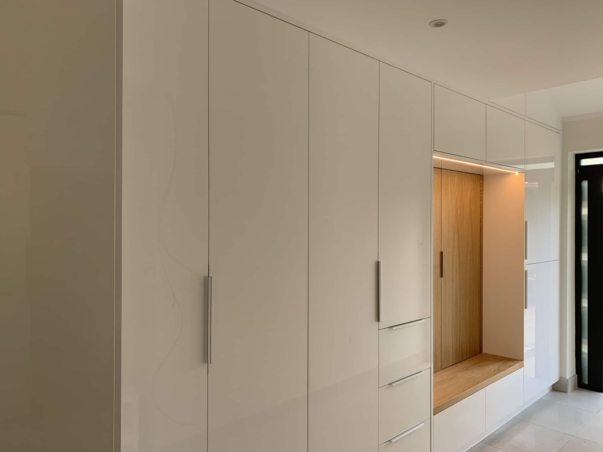 Hallway wardrobe in multi-storage room. Coat hang area with bench. White high gloss finish.